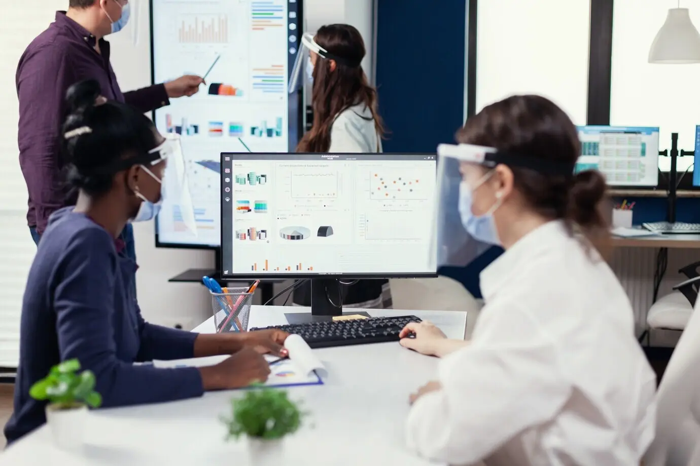 Сотрудник африканского происхождения слушает тренера на конференции по продажам во время COVID‑19. Многонациональная команда работает в компании в условиях новой нормальности, соблюдая социальную дистанцию во время глобальной пандемии коронавируса.