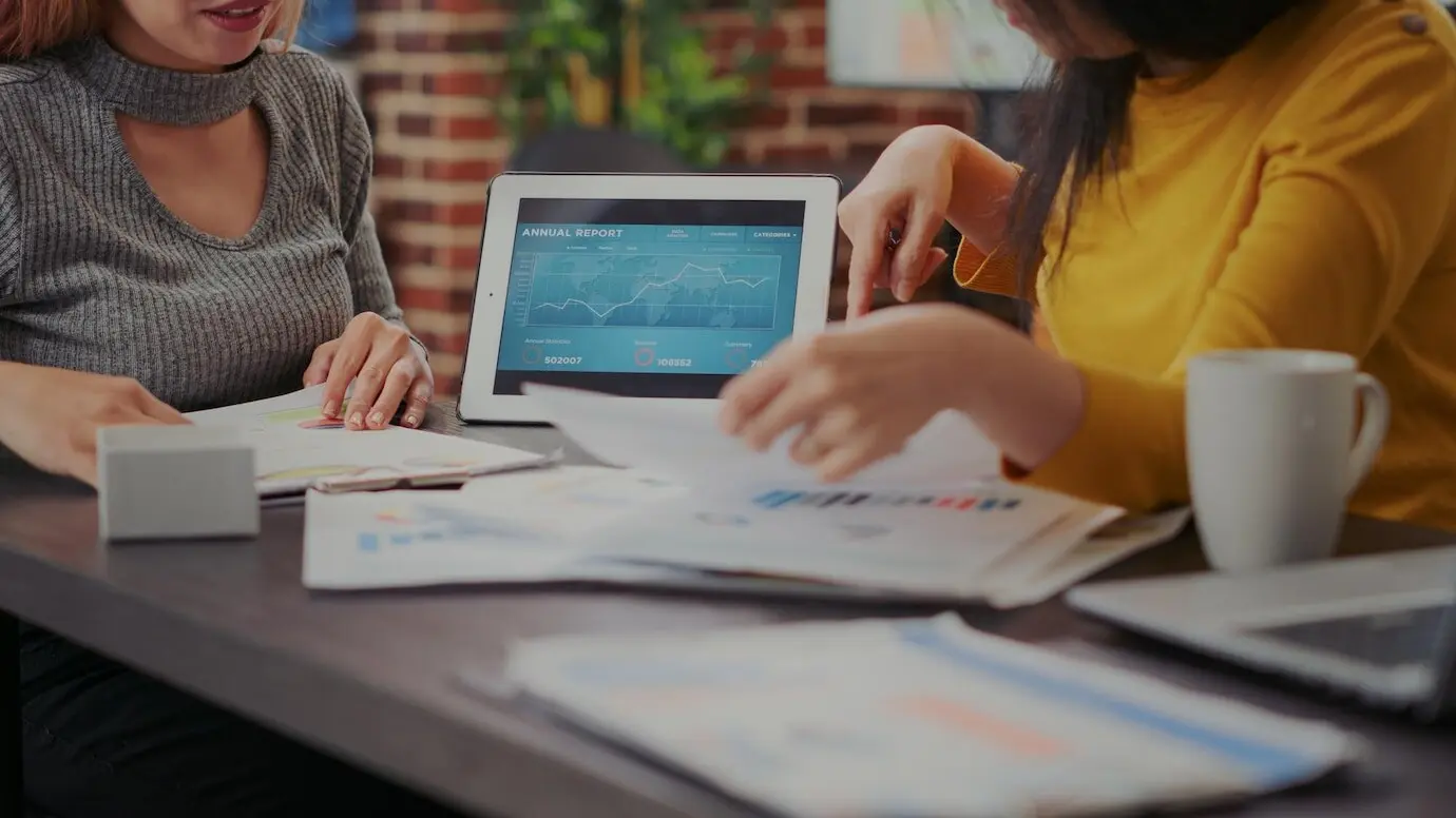 Женщины анализируют финансовый отчет на цифровом планшете, работая над ростом бизнеса. Коллеги используют анализ данных о продажах для планирования инвестиций в развитие. Устройство со статистикой. Крупный план.